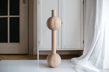 A handmade wooden furniture leg with two spheres, crafted from unfinished raw wood, displayed in an indoor setting.