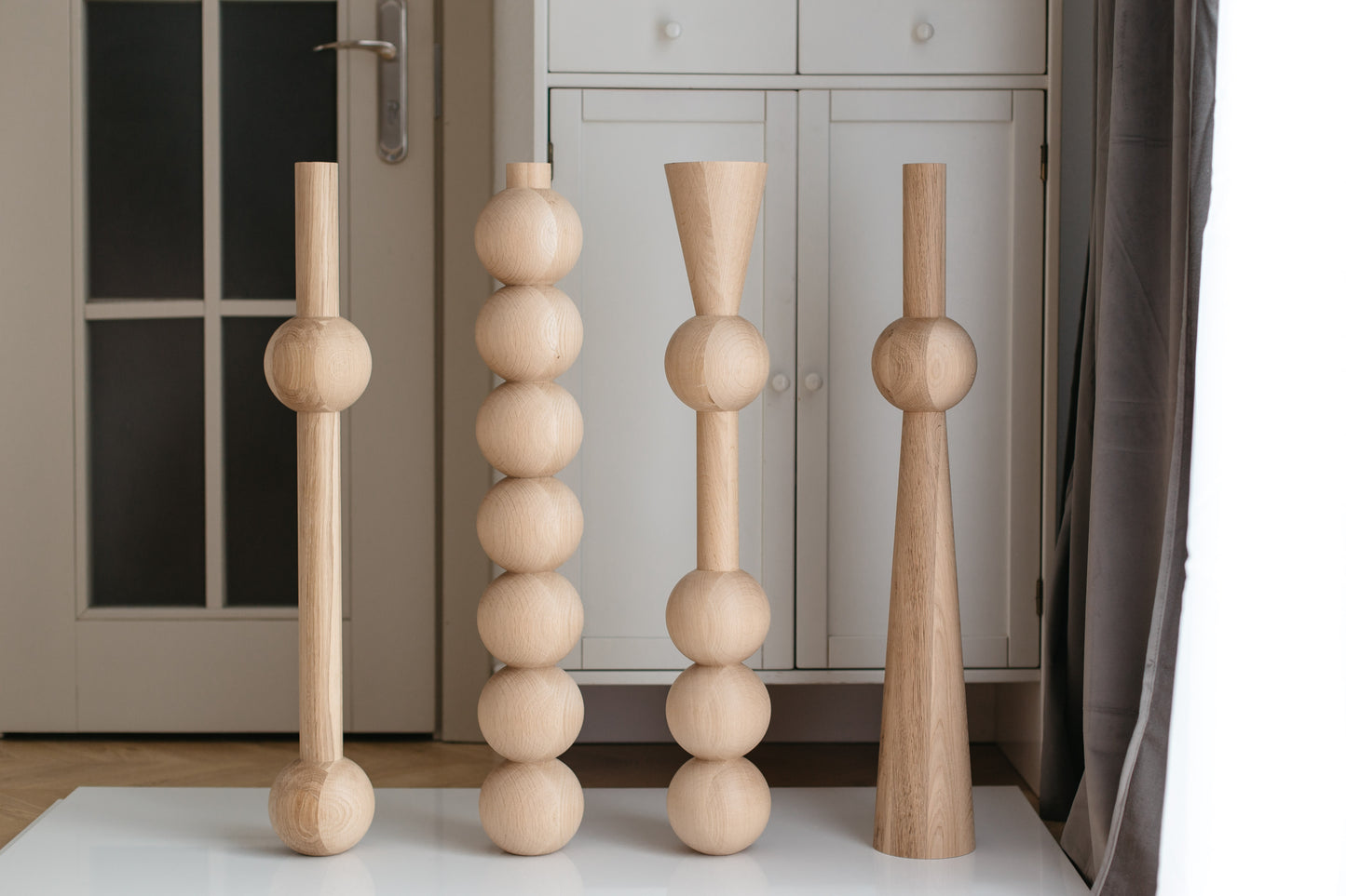 Four wooden candle holders of different designs on a white surface.